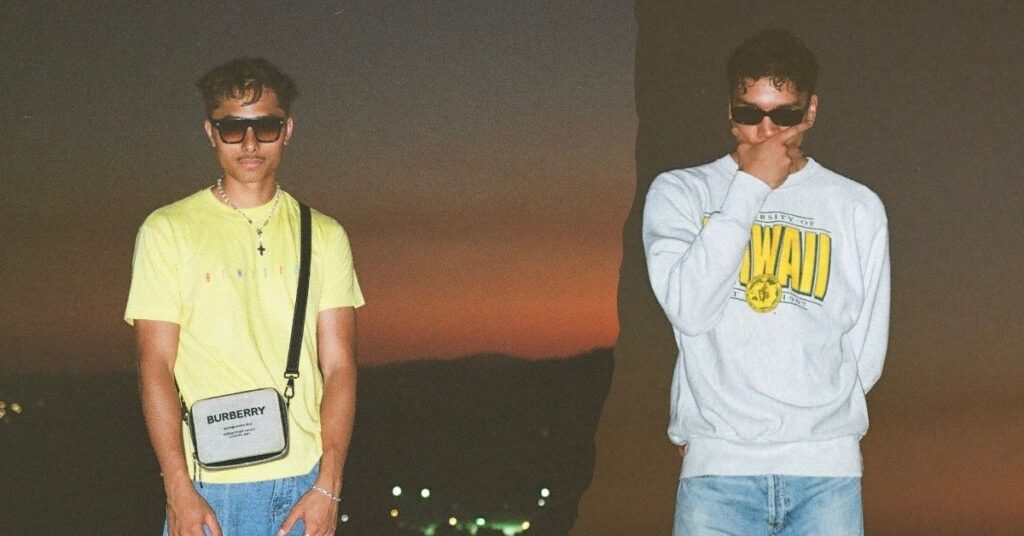 Franskiiz and Lelz posing together at sunset, highlighting urban fashion with a Burberry bag and a University of Hawaii sweatshirt